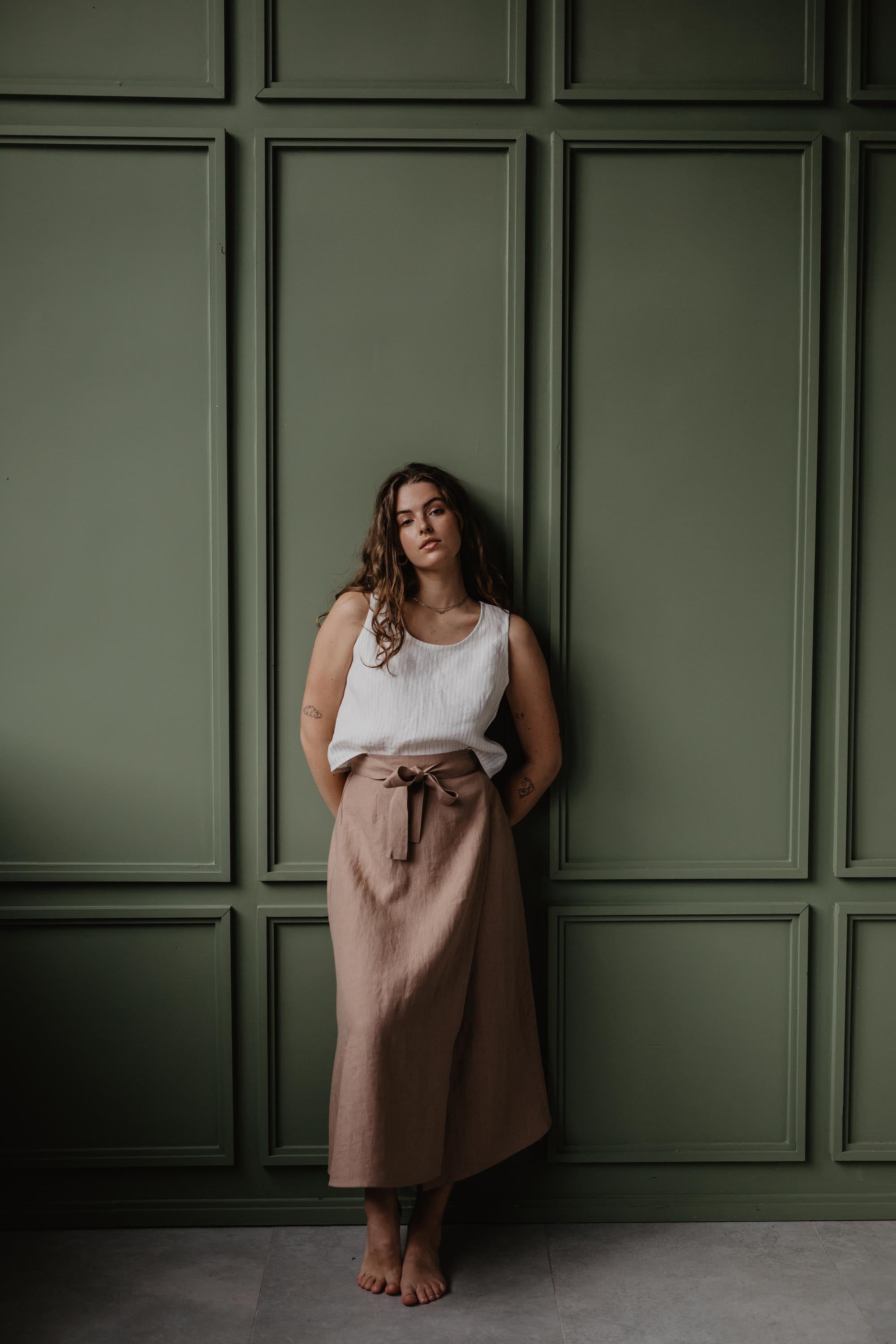 Women Leaning On Green Wall Wearing A Dusty Rose Linen Wrap Skirt