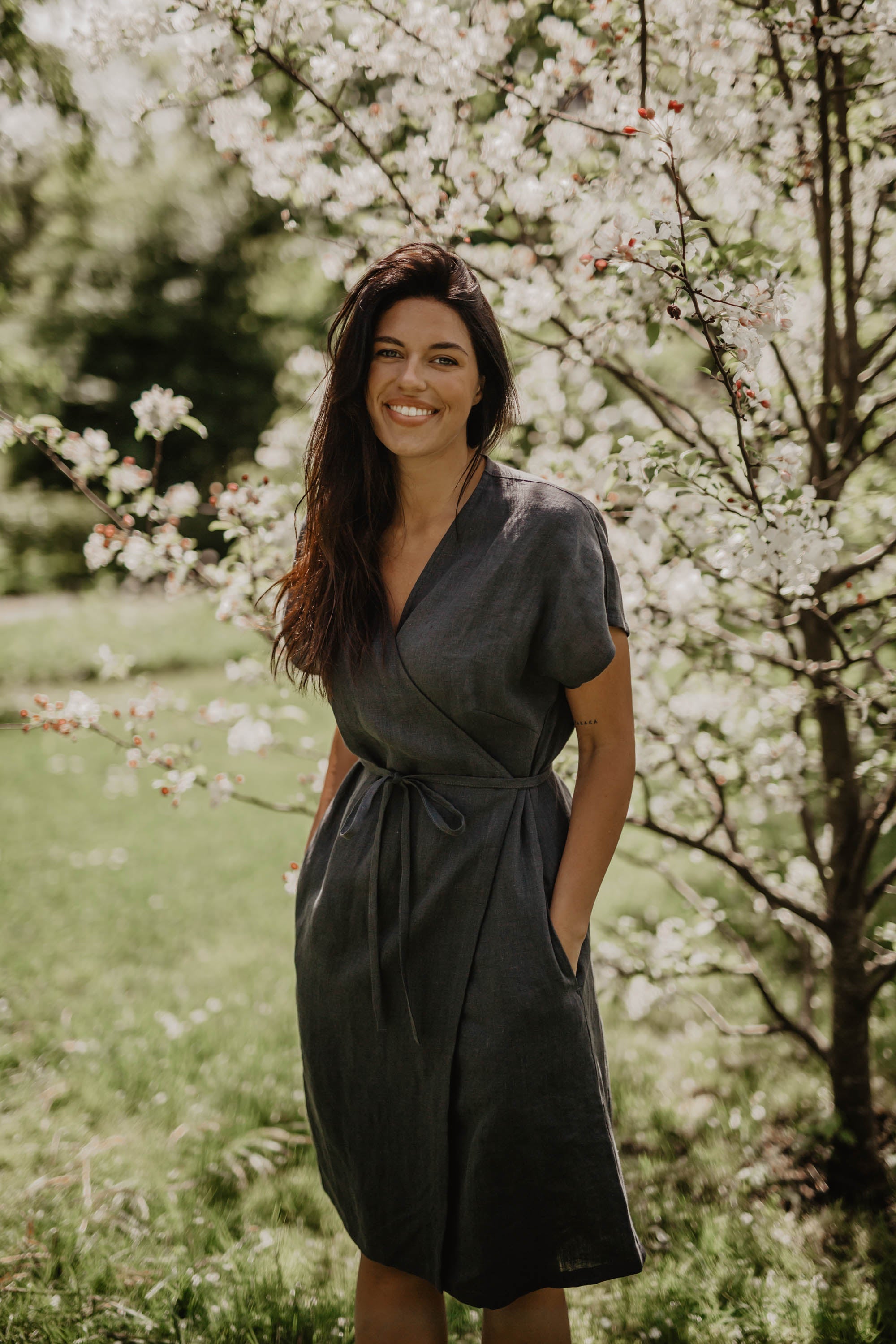 Women Wearing A Black Linen Wrap Dress Standing Next To A Blossoming Tree