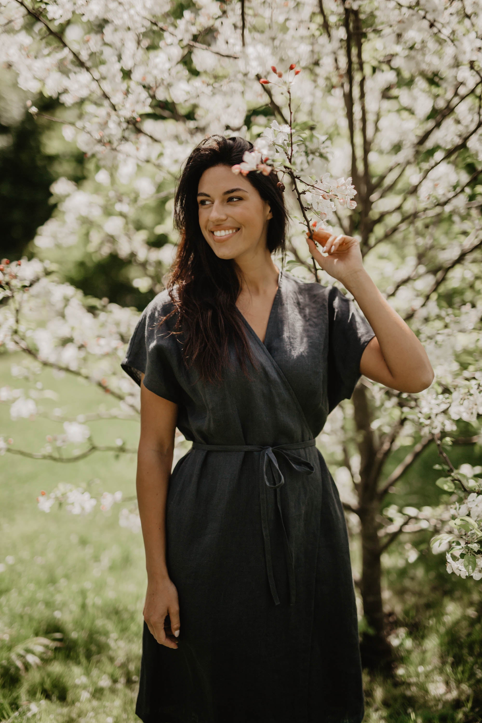 Women Holding A Blossoming Branch Wearing A Black Linen Wrap Dress