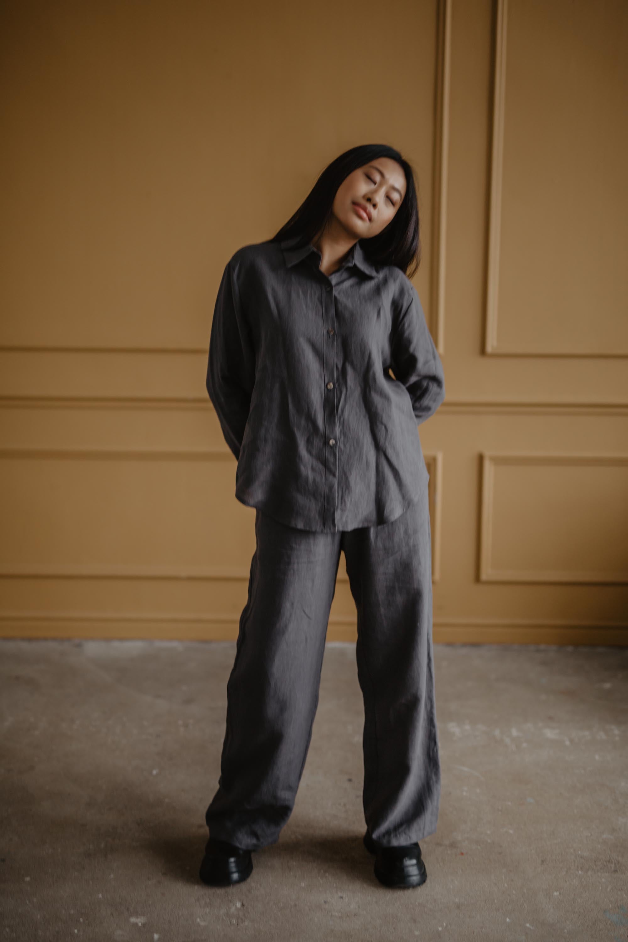 Woman Posing In Bronze Romm Wearing A Grey Casual Linen Shirt And Dark Linen Pants