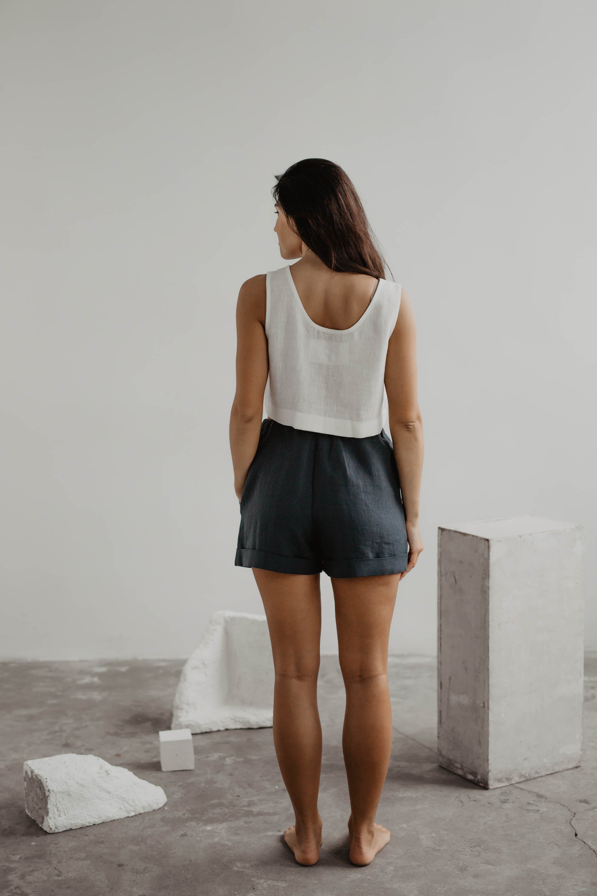 Back Of Woman Wearing Charcoal Linen Shorts With A White Linen Top In A Gallery