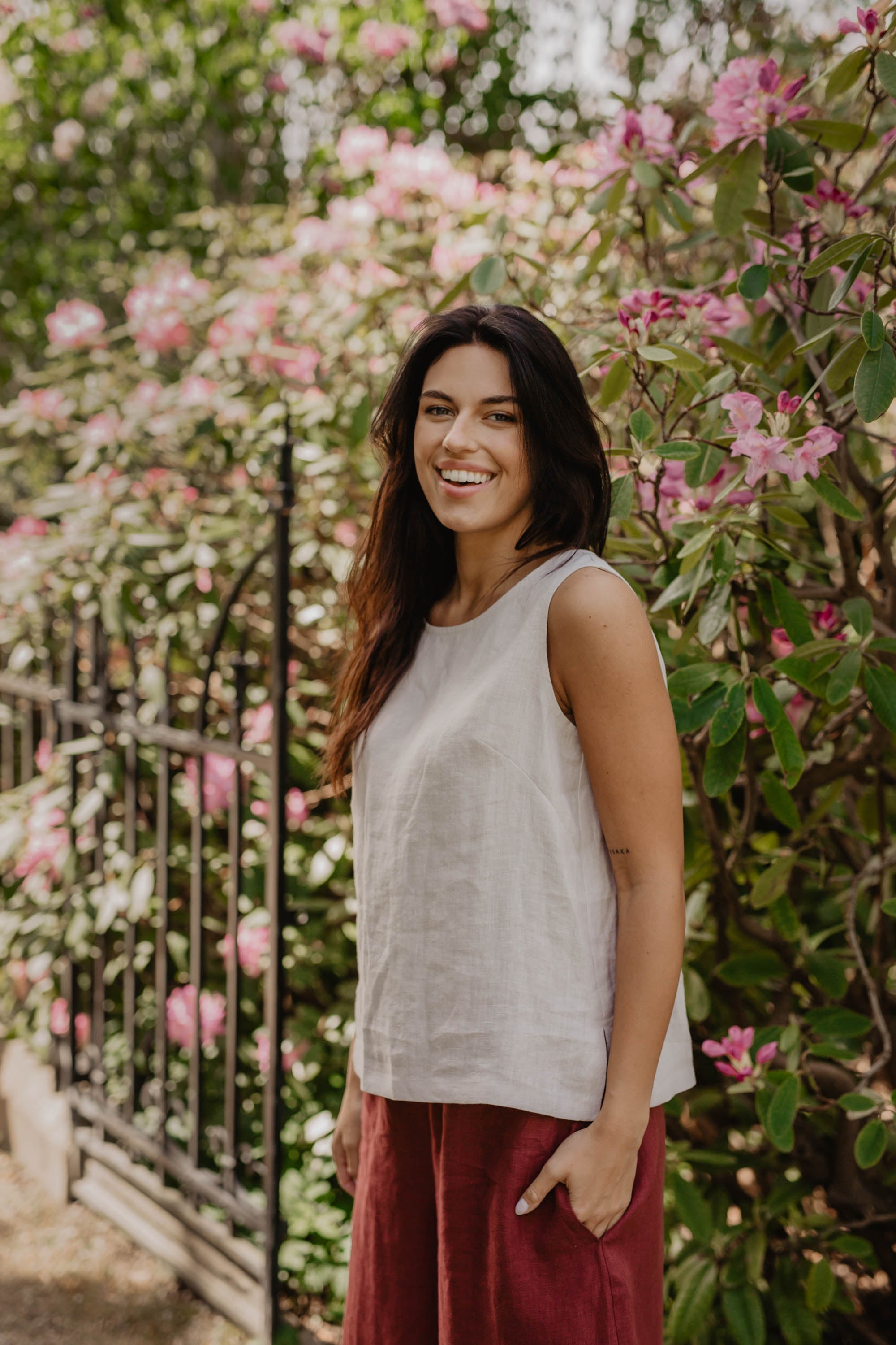 Woman In Flower Garden Wearing A White Linen Top and Red Linen Pants